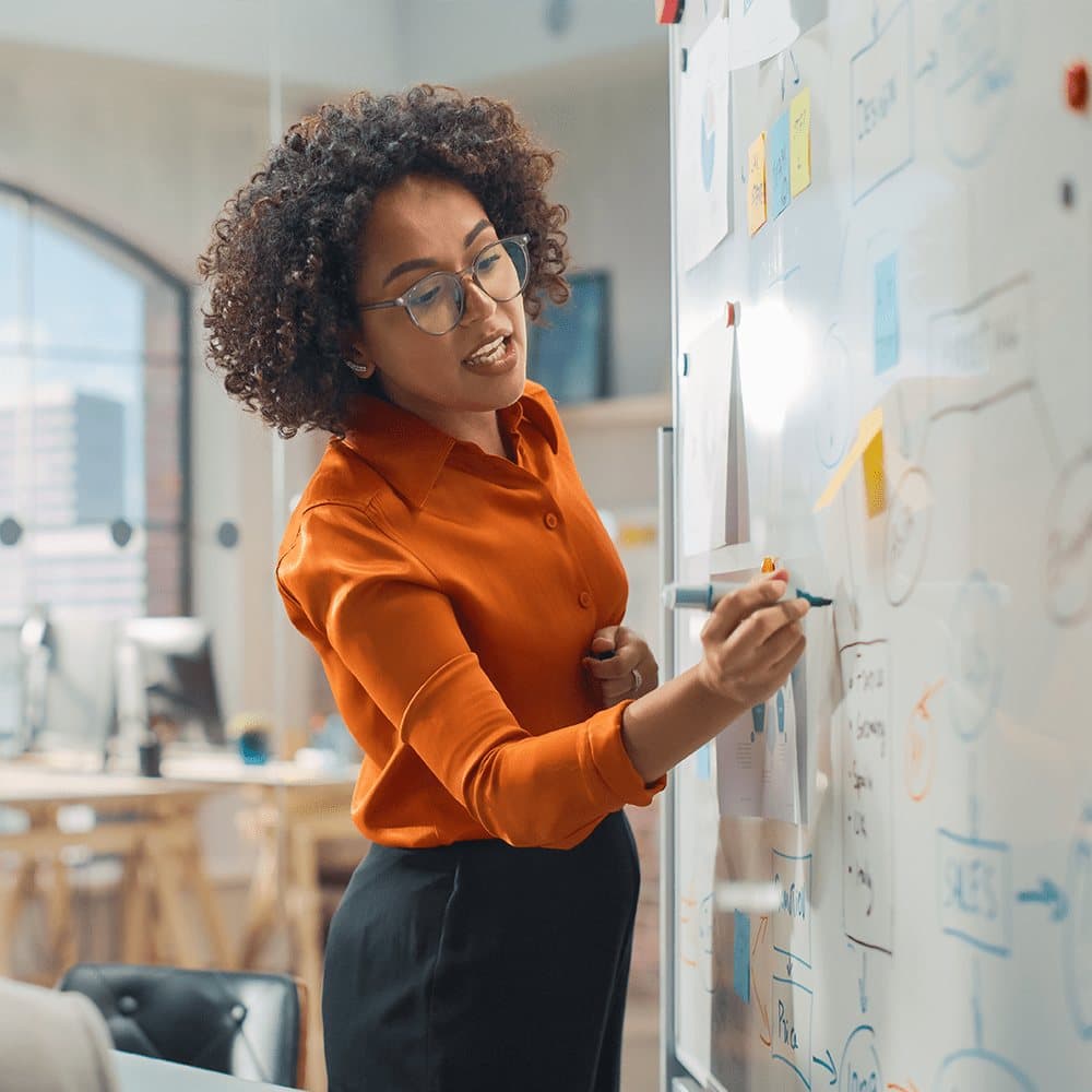 A facilitator writing on a glass whiteboard covered in sticky notes.