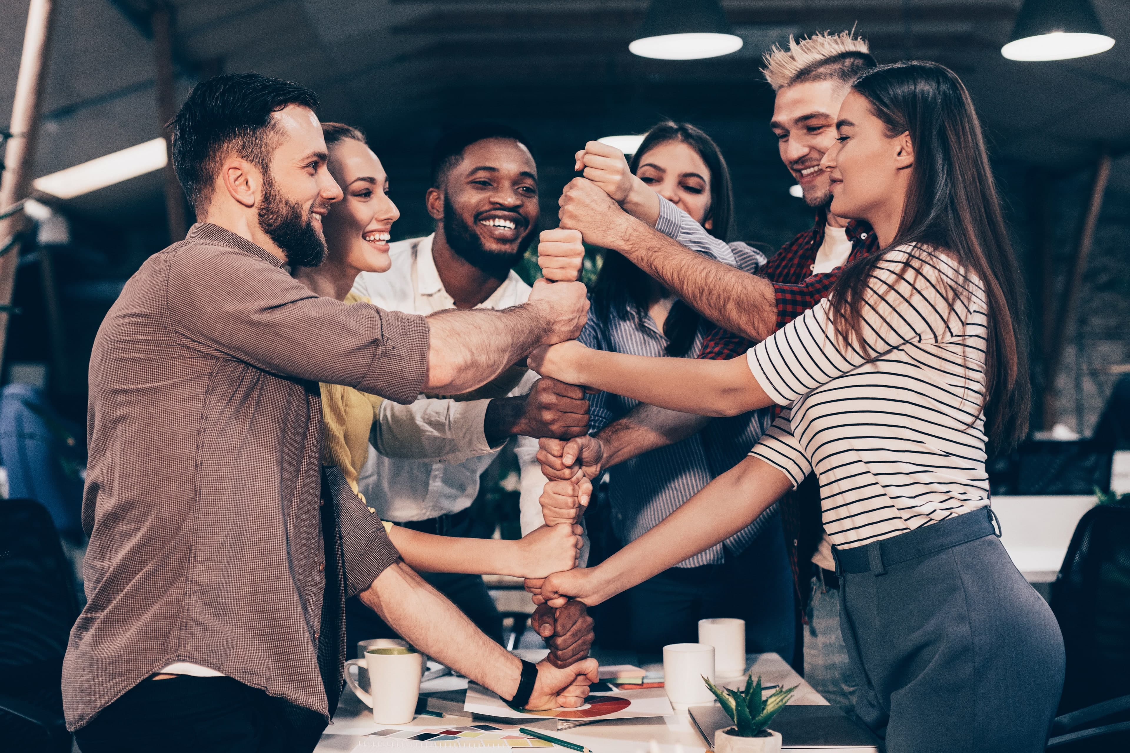 Six smiling teammates stacking their fists over an office table.