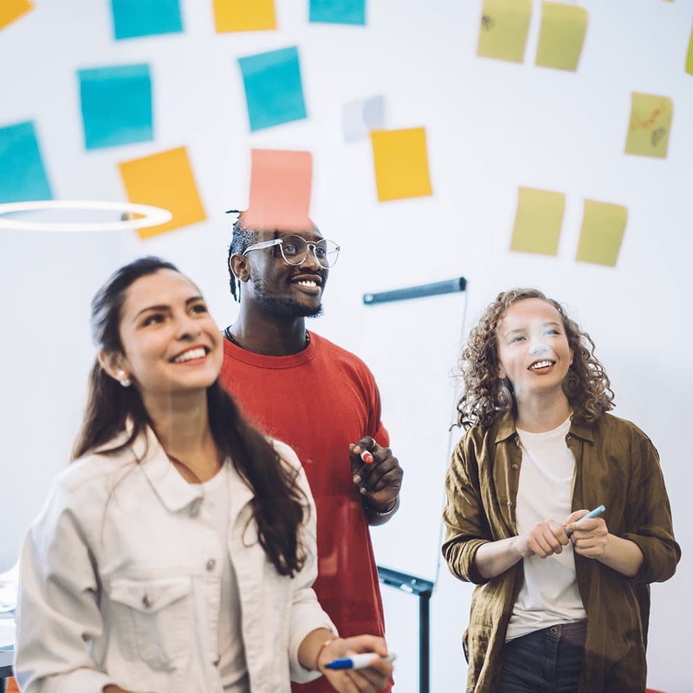 Colleagues smiling in front of a wall of sticky notes.